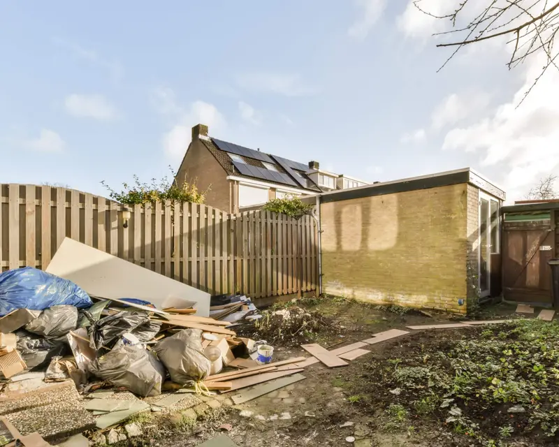 Overgrown backyard with old roof tiles and debris before clearance
